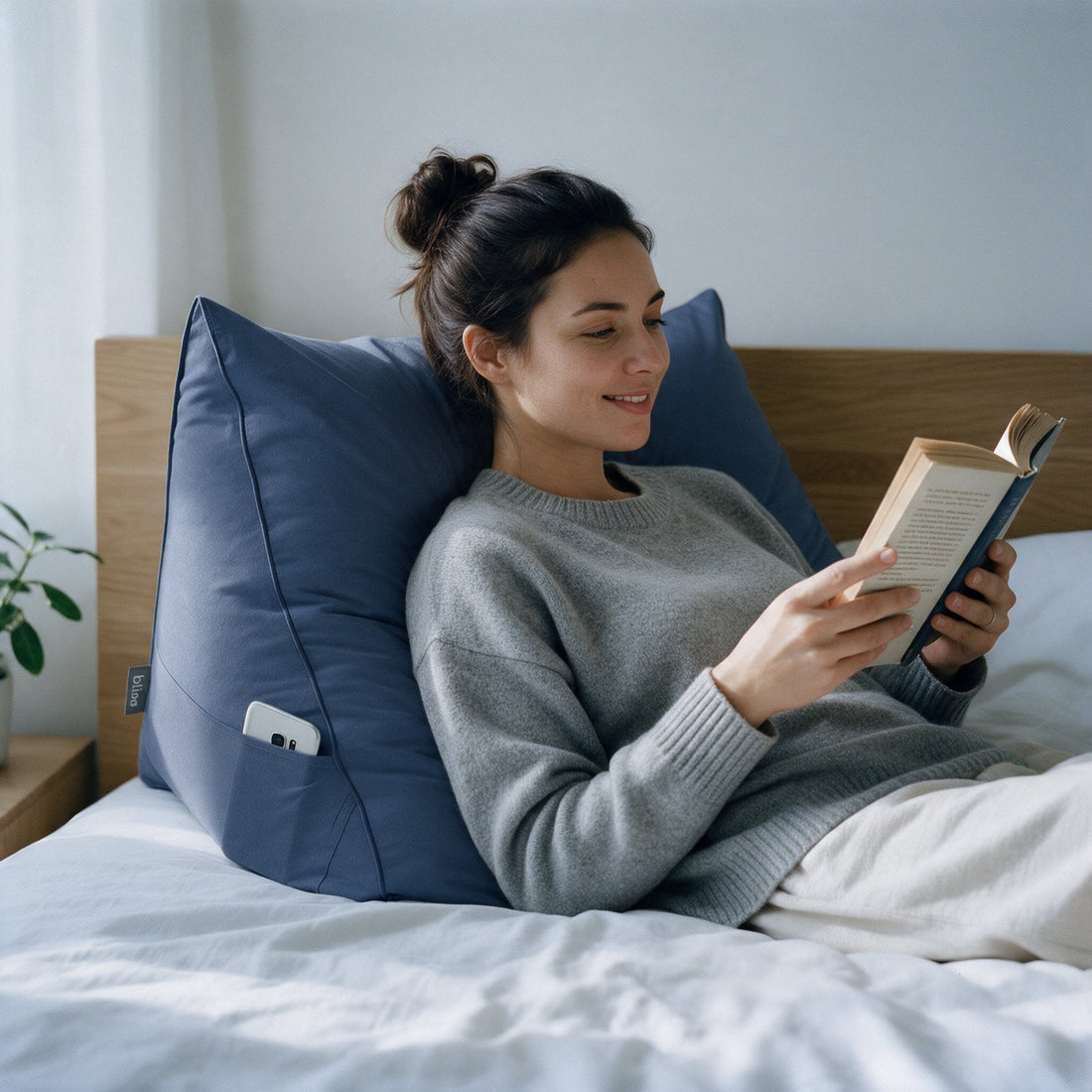 Vrouw leest een boek in bed tegen het Bline leeskussen in Blauw