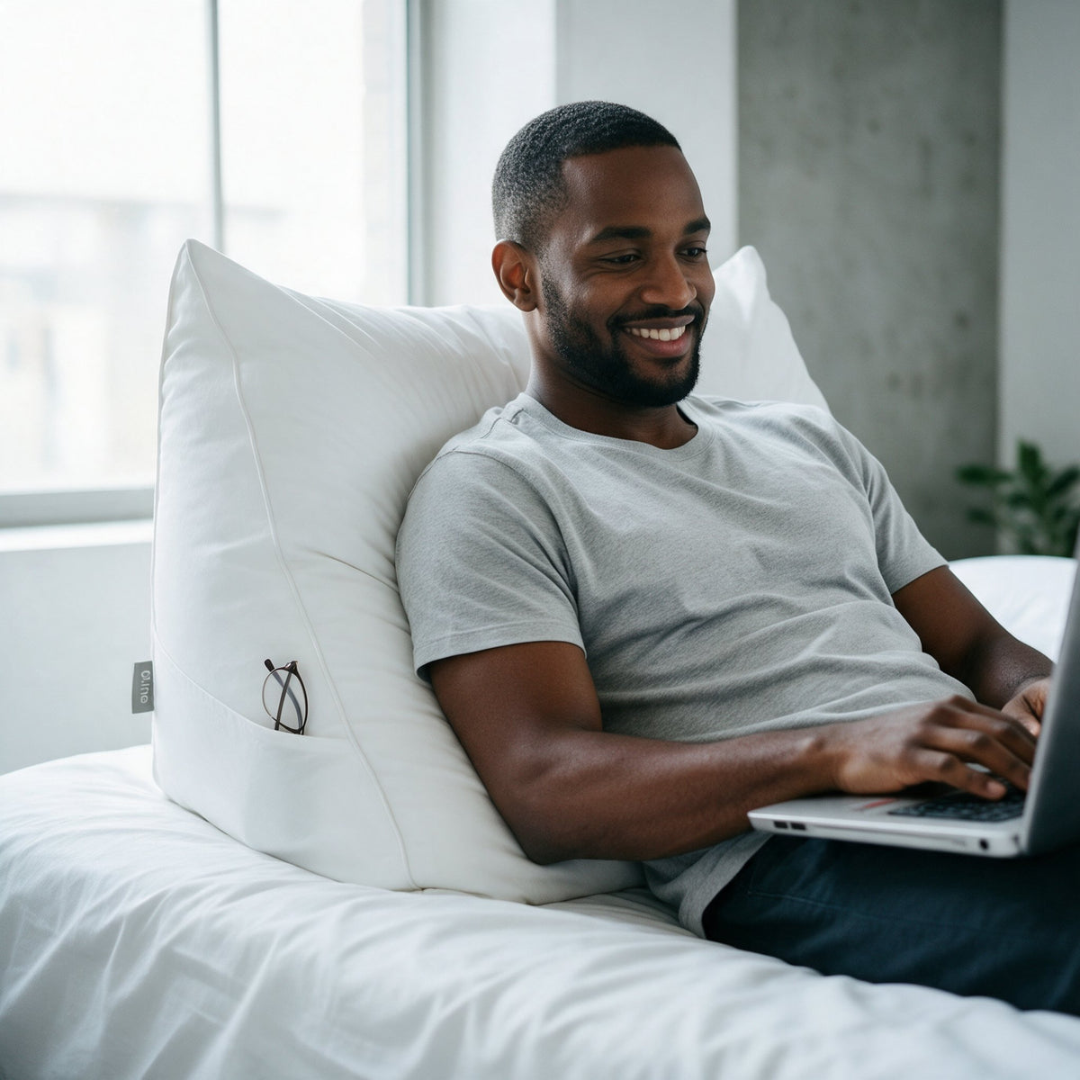 Man leunt tegen het leeskussen Bline, kleur Wit, met een laptop op schoot