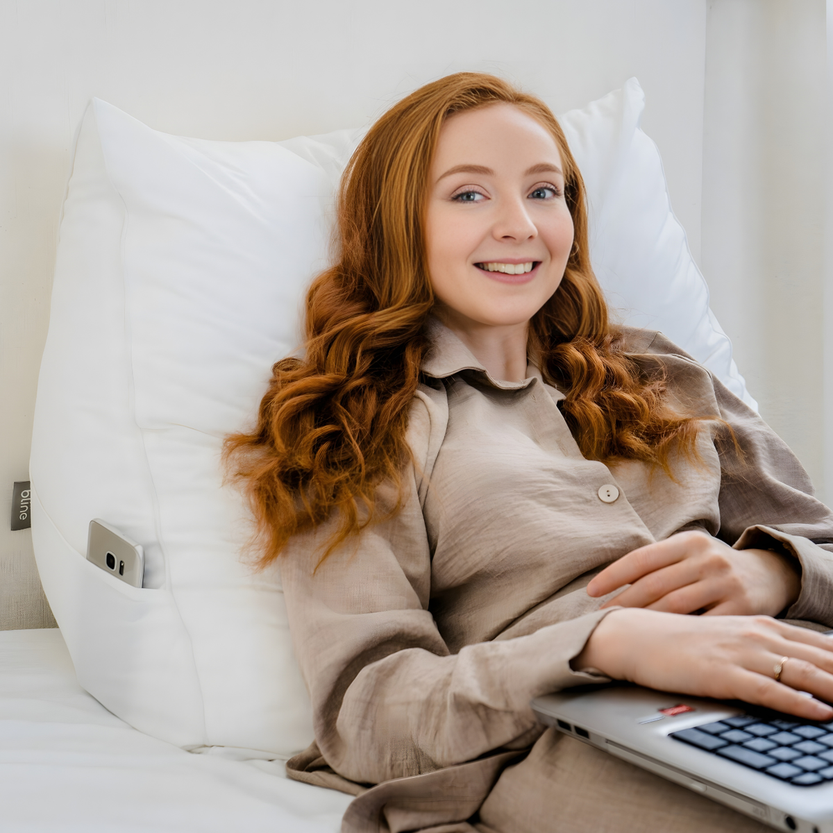 Vrouw met laptop tegen het leeskussen Bline, kleur Wit, met haar telefoon in het zijvak