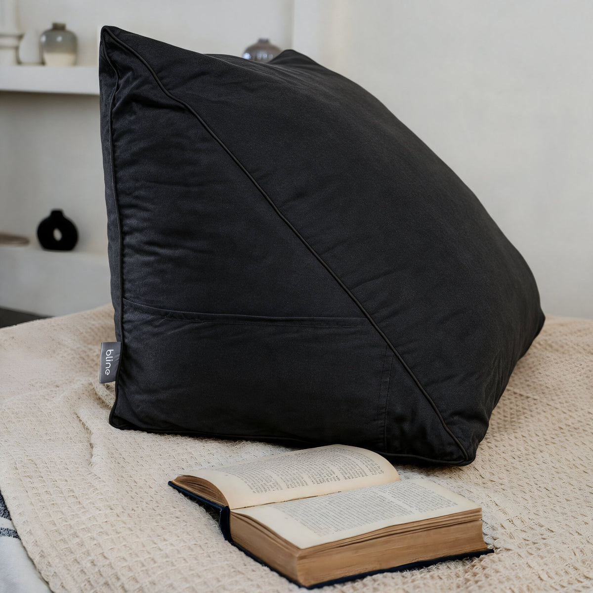 Leeskussen Bline, kleur Zwart, op een bed met een opengeslagen boek