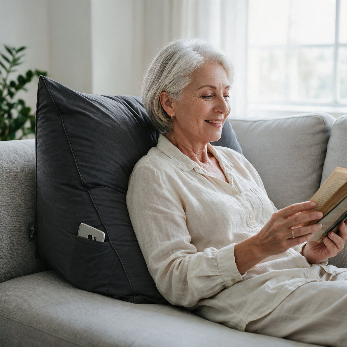 Vrouw leest een boek tegen het leeskussen Bline, kleur Zwart, op de bank
