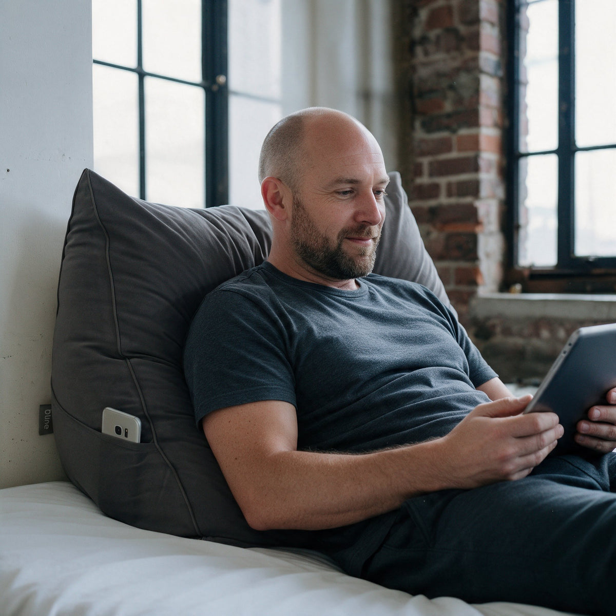 Man met tablet tegen het leeskussen Bline, kleur Zwart, met telefoon in het zijvak